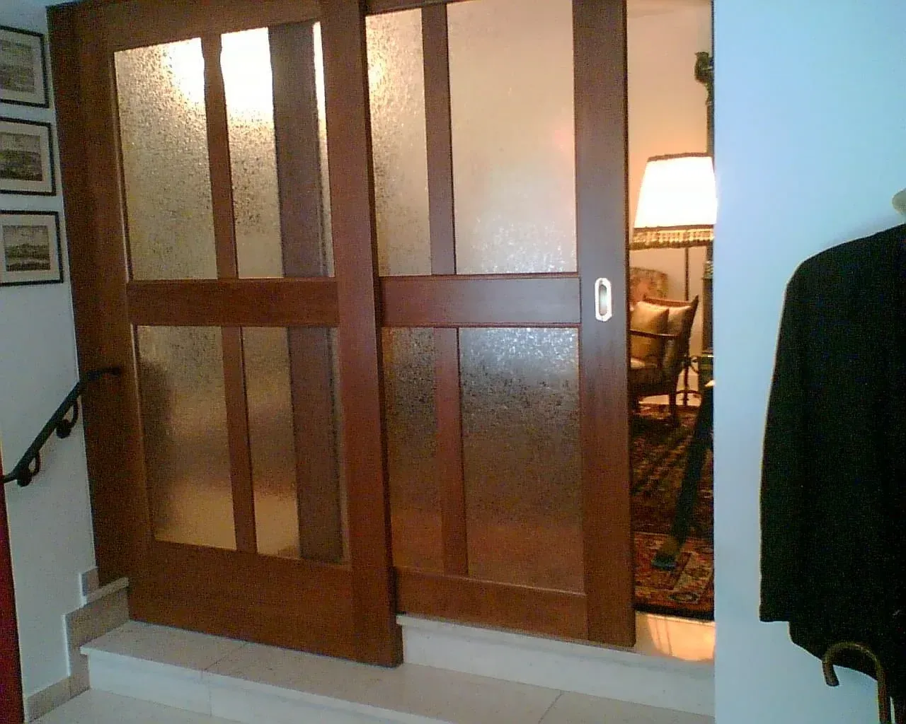 Holzschiebetüren, Milchglasscheiben, teilweise geöffnet, geben den Blick auf einen beleuchteten Raum frei.