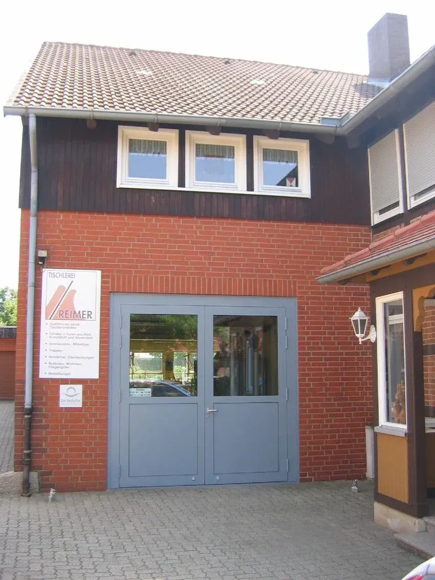 Rotes Backsteingebäude mit blauen Türen, drei Fenstern und einem braunen Dach.