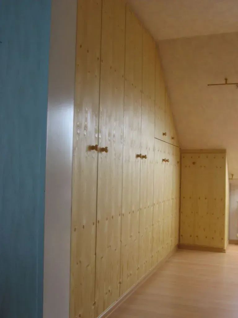 Helle Holzschränke säumen eine schräge Wand in einem Raum mit hellem Fußboden.