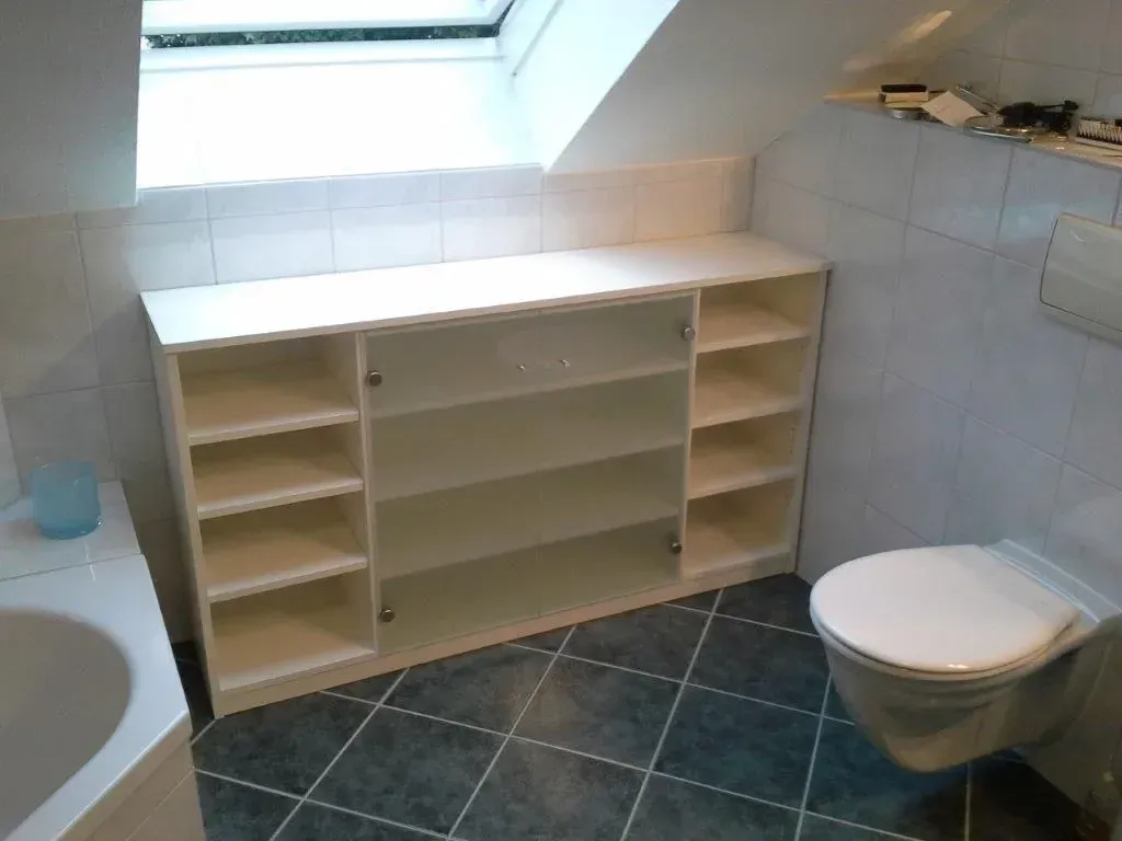 Weißes Regal in einem Badezimmer mit Dachfenster, Toilette und Badewanne.