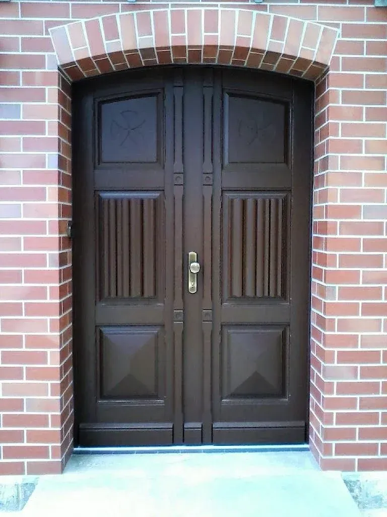 Braune Doppeltüren mit Zierpaneelen in einem roten Backsteingebäude mit gewölbtem Backsteindach.