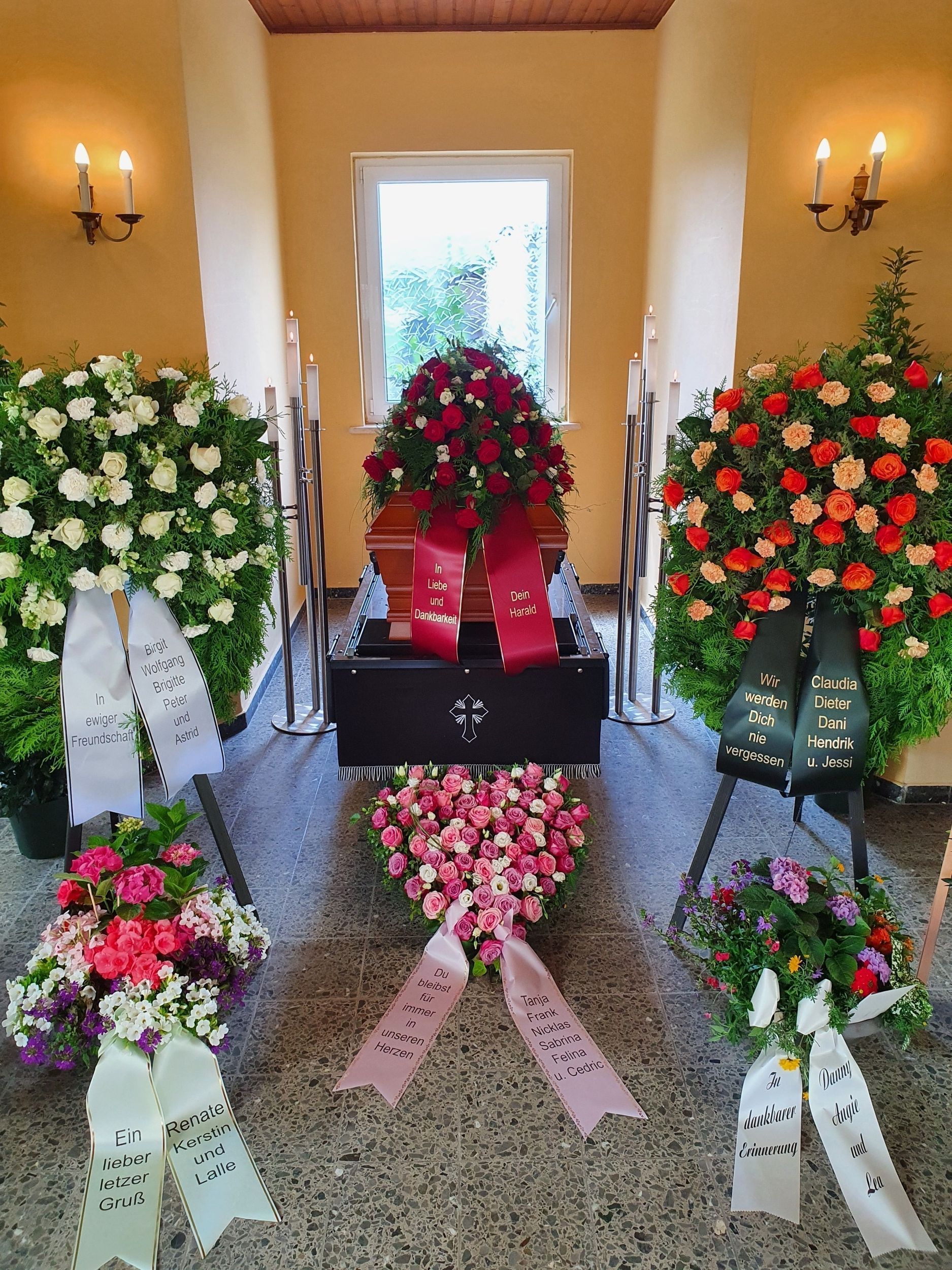 Ein Sarg bei einer Beerdigung, umgeben von Blumenarrangements und Kränzen.