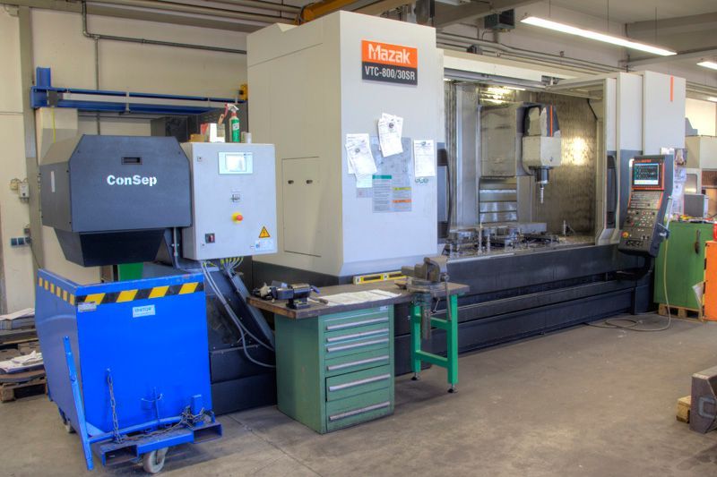 Eine große Mazak CNC-Fräsmaschine in einer Werkstatt mit einem blauen Spänebehälter, einem grünen Werkzeugschrank 