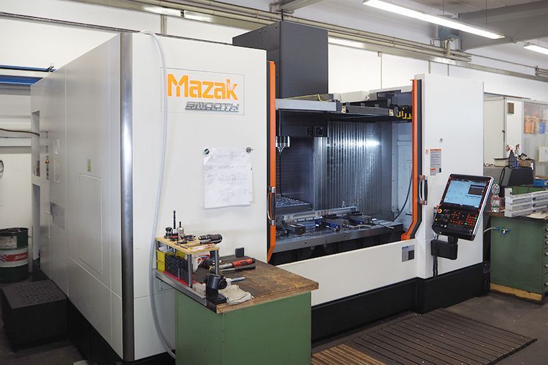 Eine weiße Mazak VTC-800/30SR CNC-Maschine in einer Werkstatt mit einem Bedienfeld auf der rechten Seite.