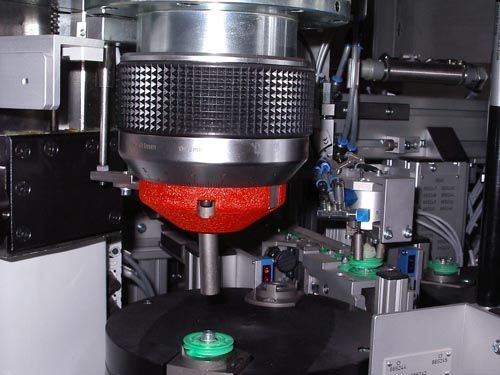 Nahaufnahme einer Industriemaschine, die ein rotes, kegelförmiges Bauteil über einer rotierenden Plattform zeigt.