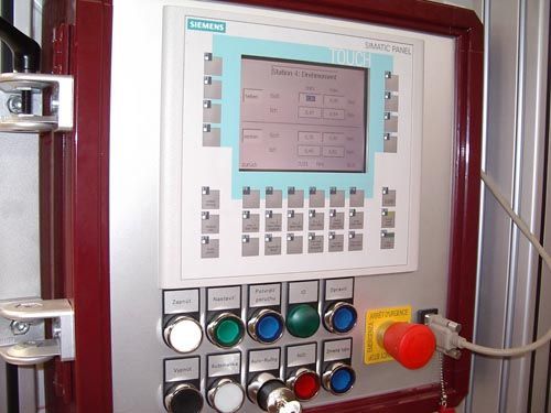 Ein Siemens-Bedienfeld mit LCD-Display, Tastatur, Tasten und einem roten Not-Aus-Schalter auf einer Metalloberfläche.