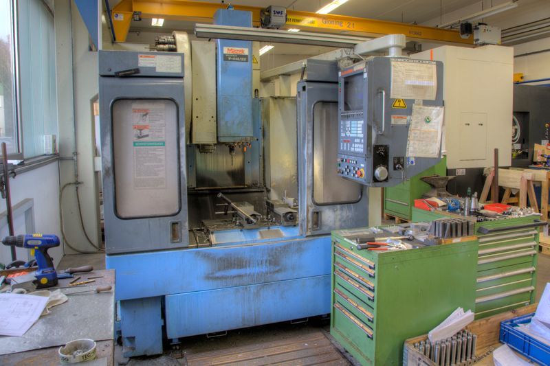 In einer Werkstatt steht eine blaue industrielle CNC-Fräsmaschine, daneben befinden sich grüne Werkzeugschränke.