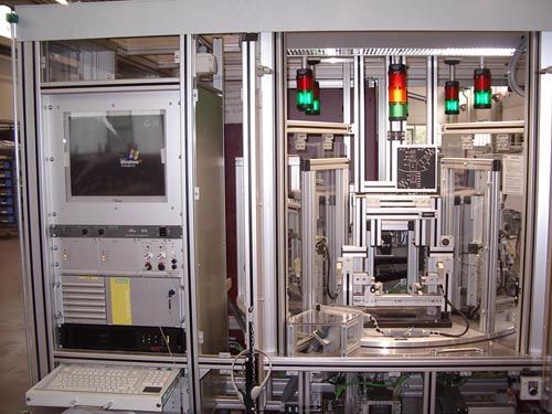 Eine industrielle Steuerstation mit Computermonitor, Tastatur und Montageausrüstung mit grünen Statusleuchten.