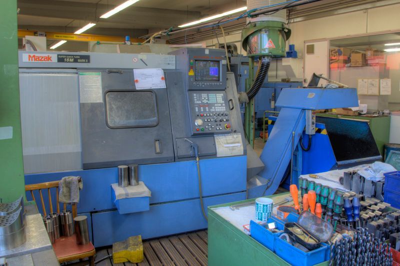 Eine Mazak CNC-Drehmaschine in einer Werkstatt, im Vordergrund eine Werkbank mit verschiedenen Werkzeugen und Geräten.