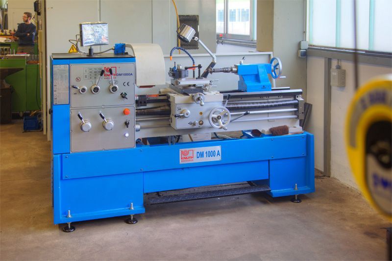 In einer Werkstatt steht eine blaue industrielle Metalldrehmaschine auf einem Betonboden.