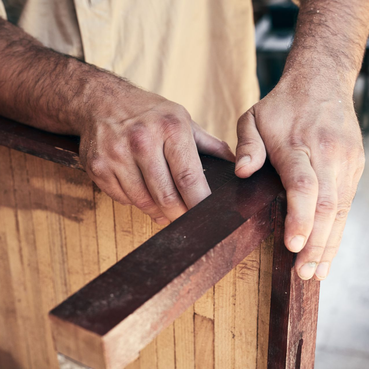 Les mains d'une personne travaillant dans la fabrication de meubles en bois, tenant une pièce de bois foncé sur un cadre en bois clair.