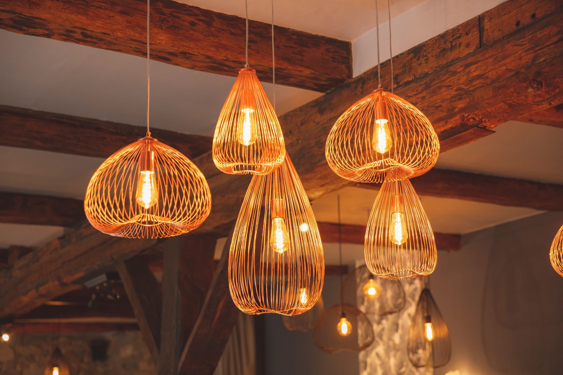 Dans une pièce à l'éclairage chaleureux, des suspensions couleur cuivre aux ampoules apparentes pendent d'un plafond en bois.