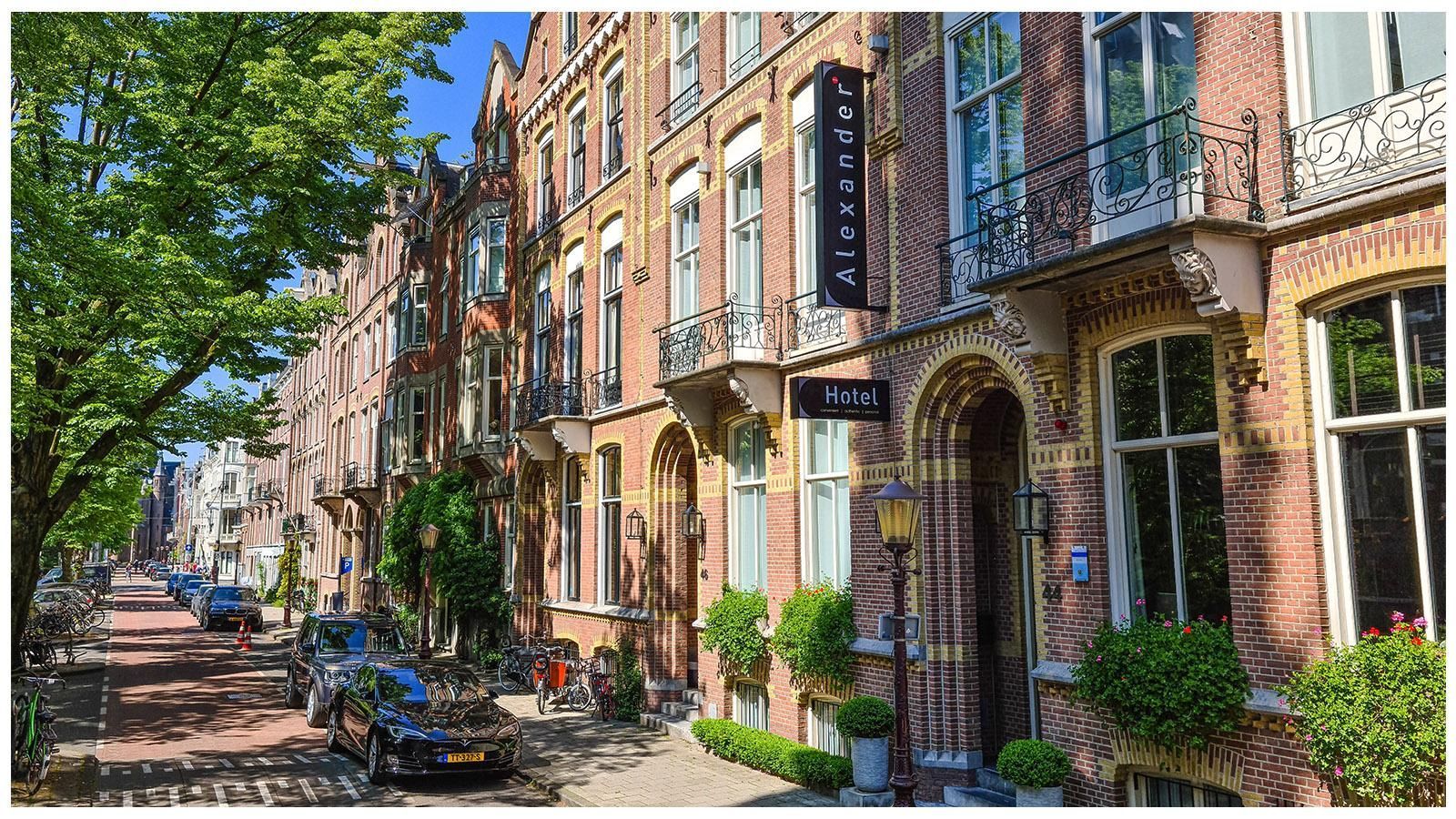 A row of brick buildings with cars parked in front of them on a sunny day.
