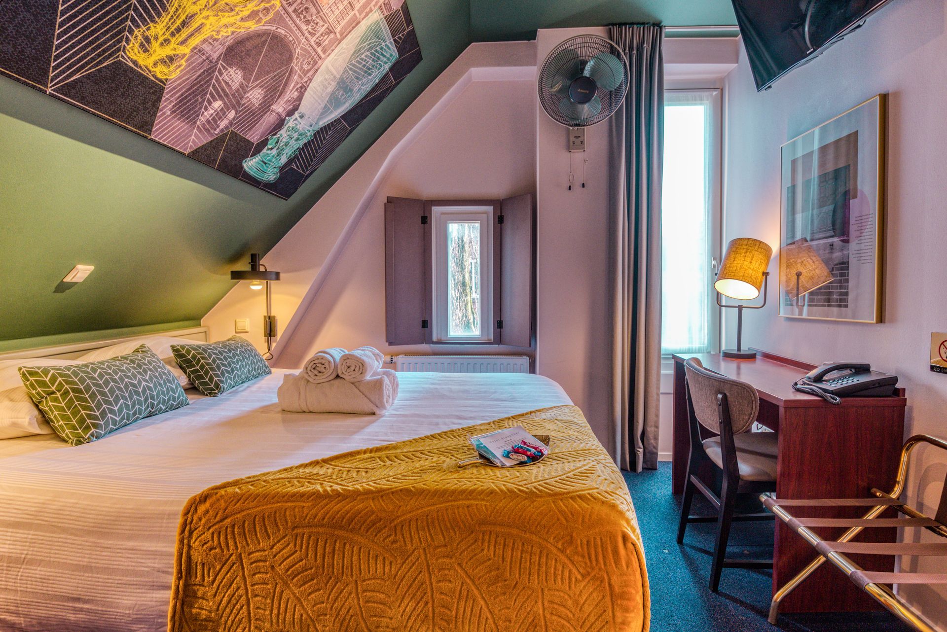 Attic room with sloped ceiling, bed with orange bedspread and a writing desk by the window