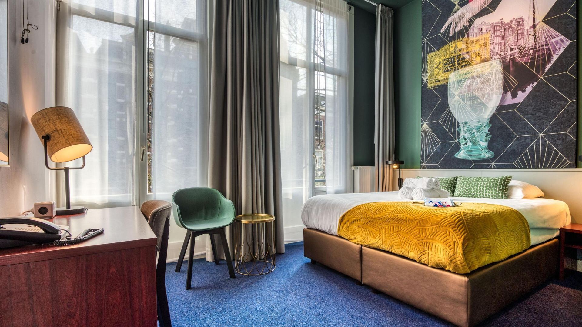 A hotel room with a bed , desk , chair and painting on the wall.