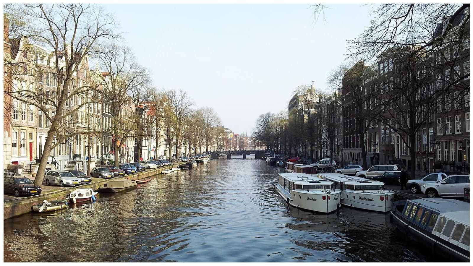 A row of boats are docked in a canal surrounded by buildings