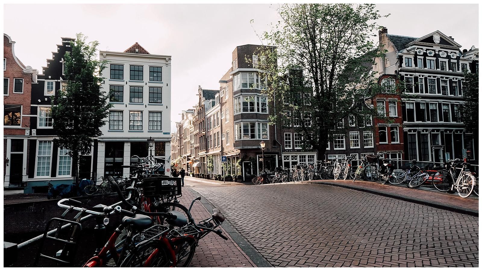 A row of bicycles are parked on the side of a cobblestone street.