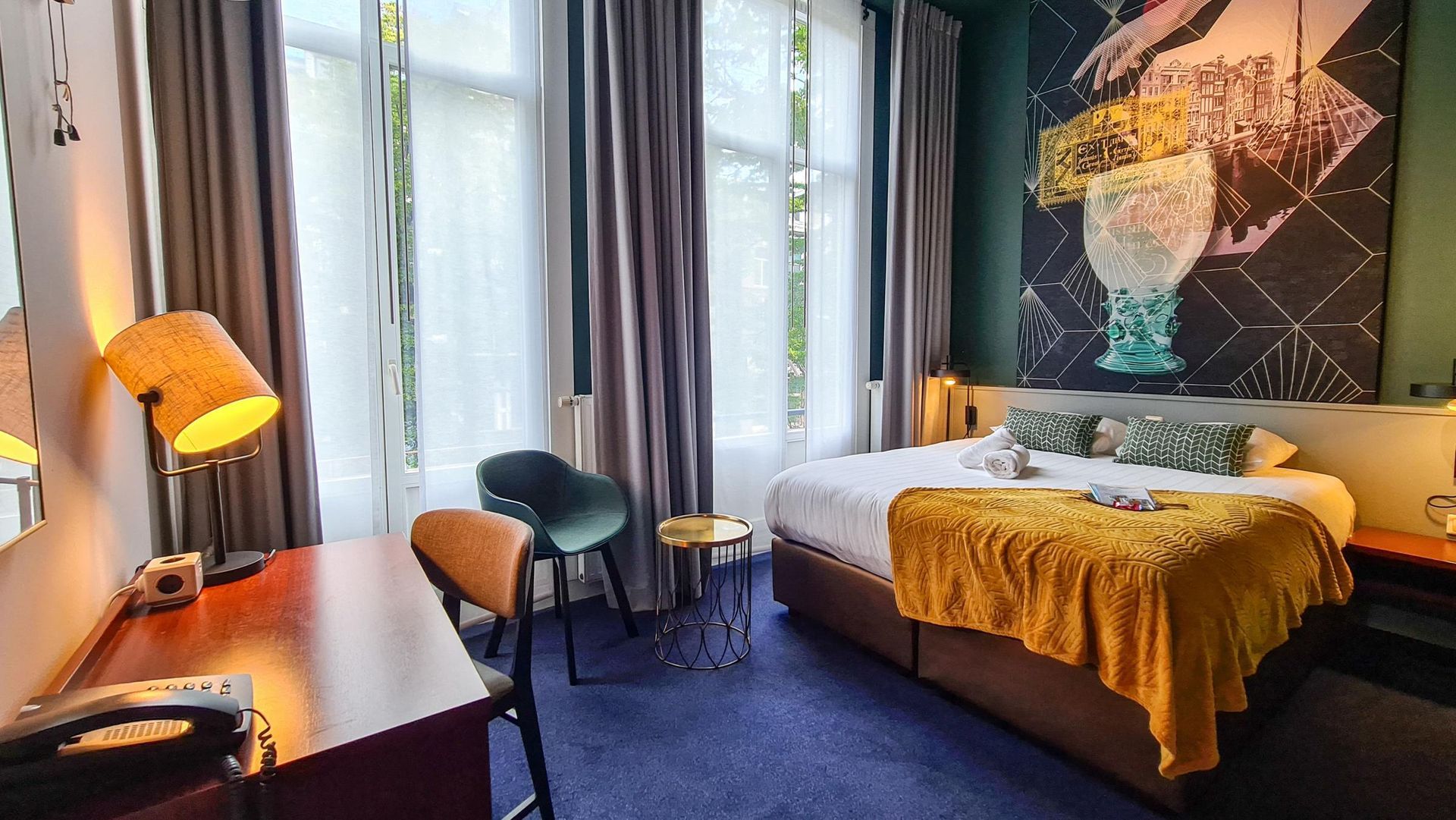 A hotel room with a bed , desk , chair and painting on the wall.