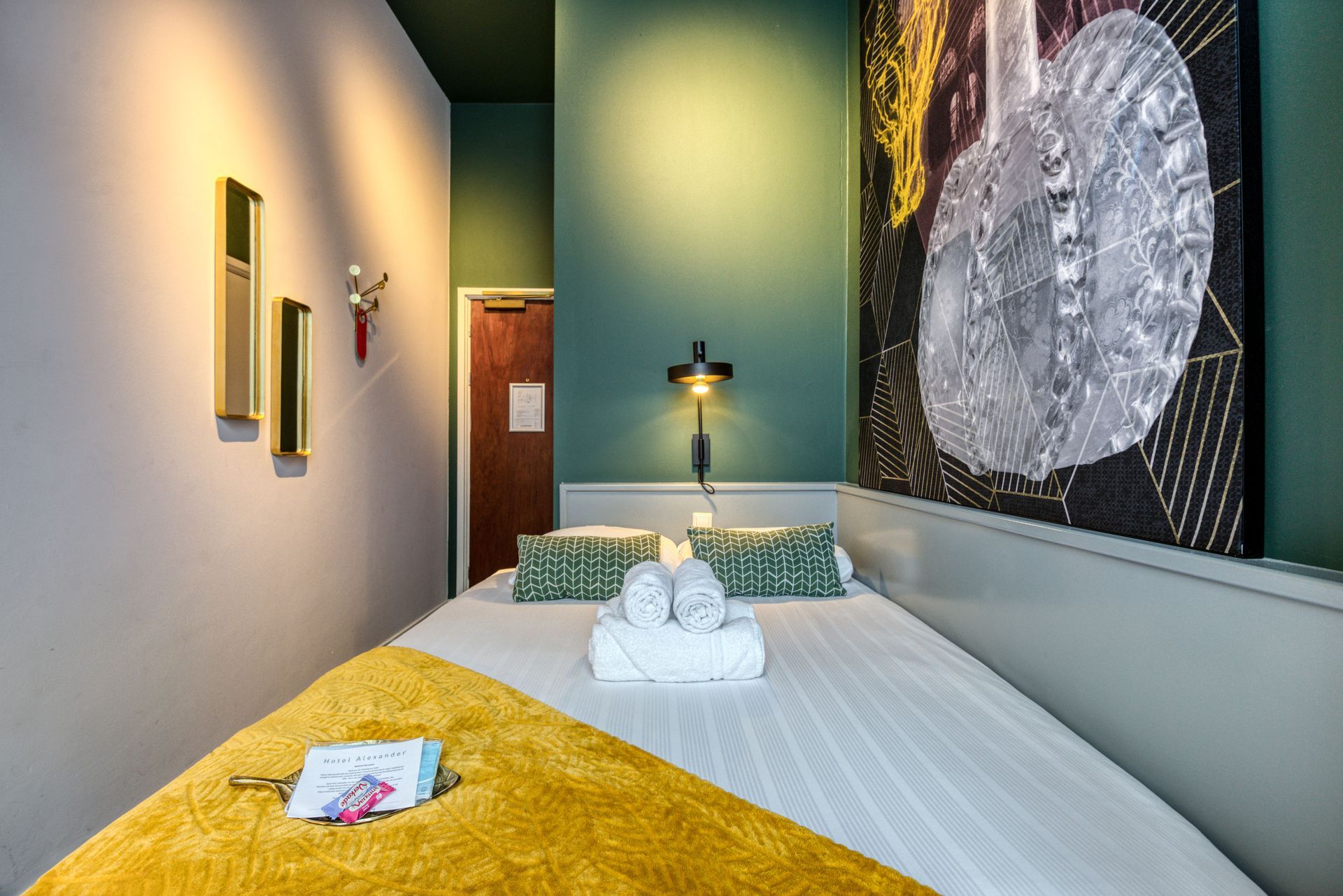 Hotel room bed with folded towels and a large art piece on a teal wall