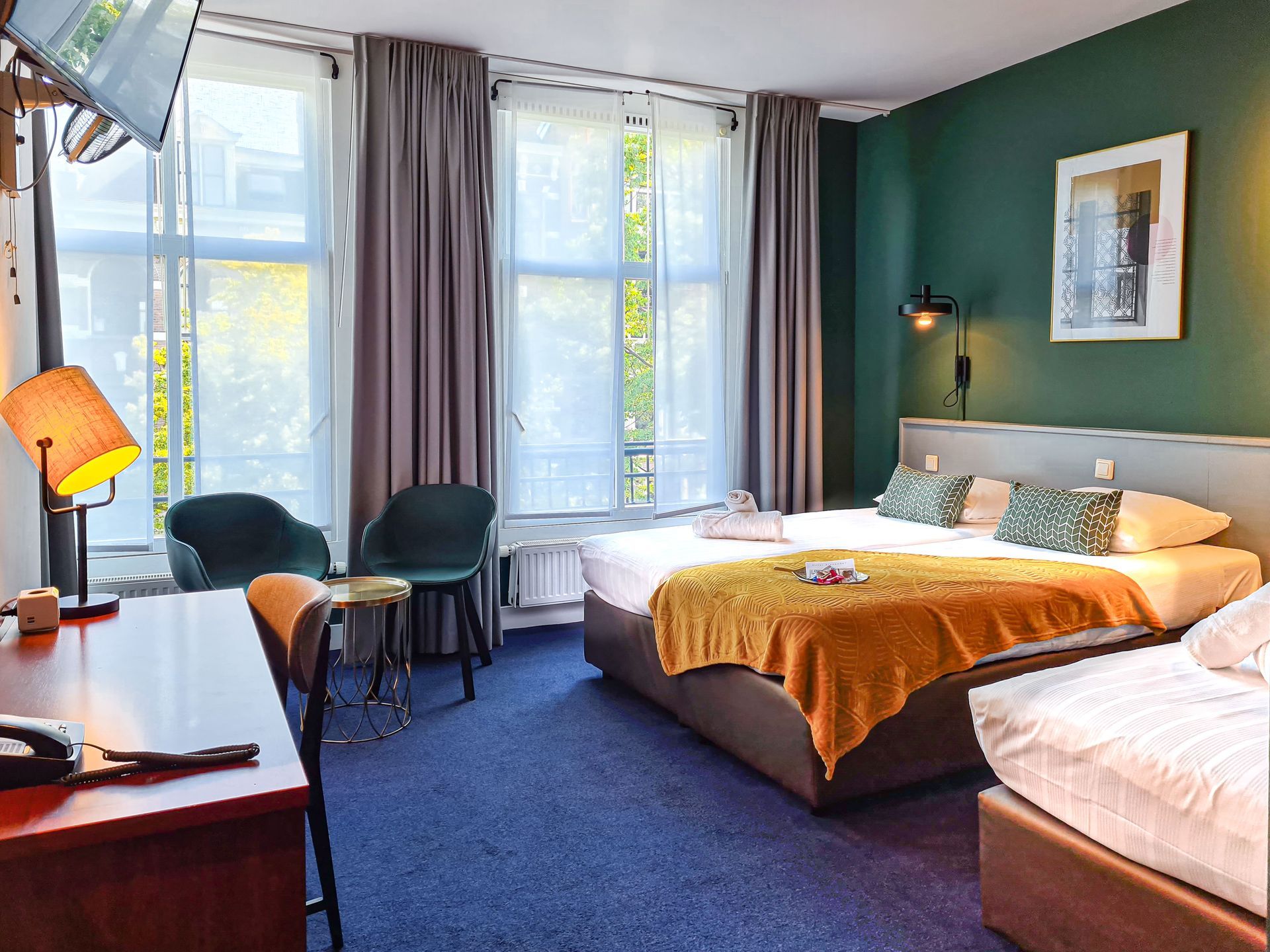 Hotel room with a a double bed and a single bed, armchairs and tall windows with curtains