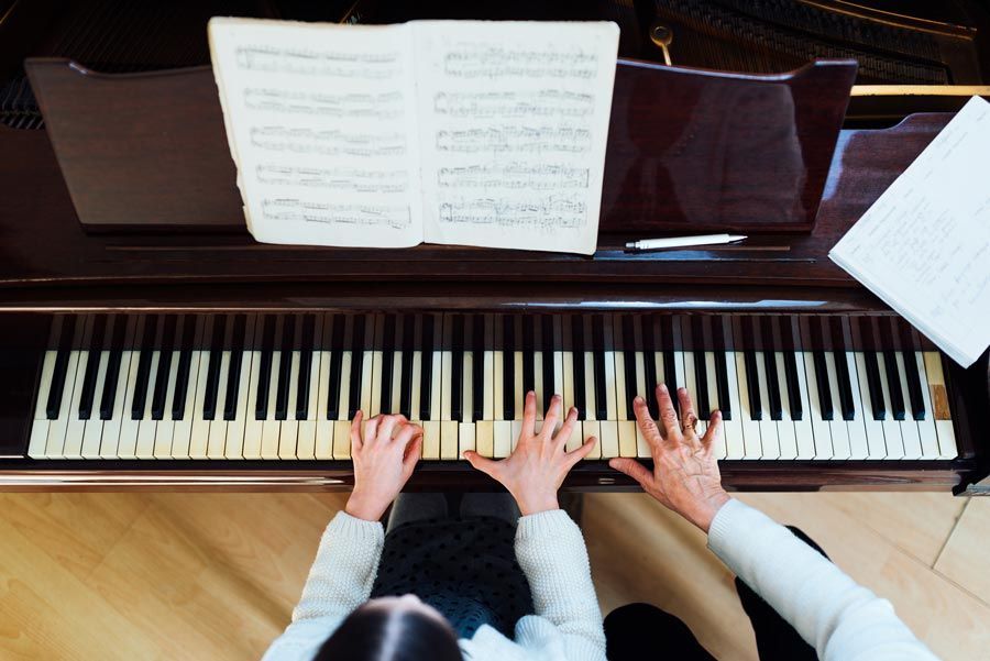 Des mains d'enfant et d'adulte sur les touches du piano, jouant de la musique à partir de partitions posées sur le pupitre.