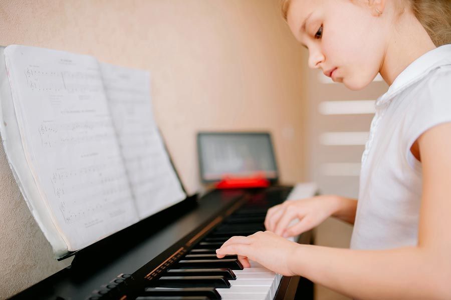 Jeune fille jouant du piano, lisant une partition, pièce aux tons clairs.