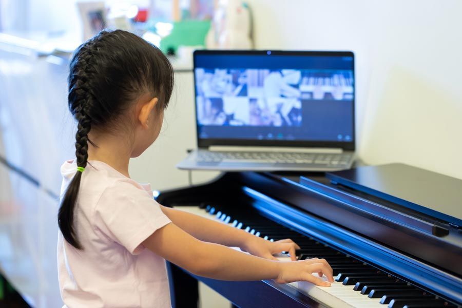 Jeune fille jouant du piano, suivant un cours en ligne sur son ordinateur portable, les mains sur les touches.