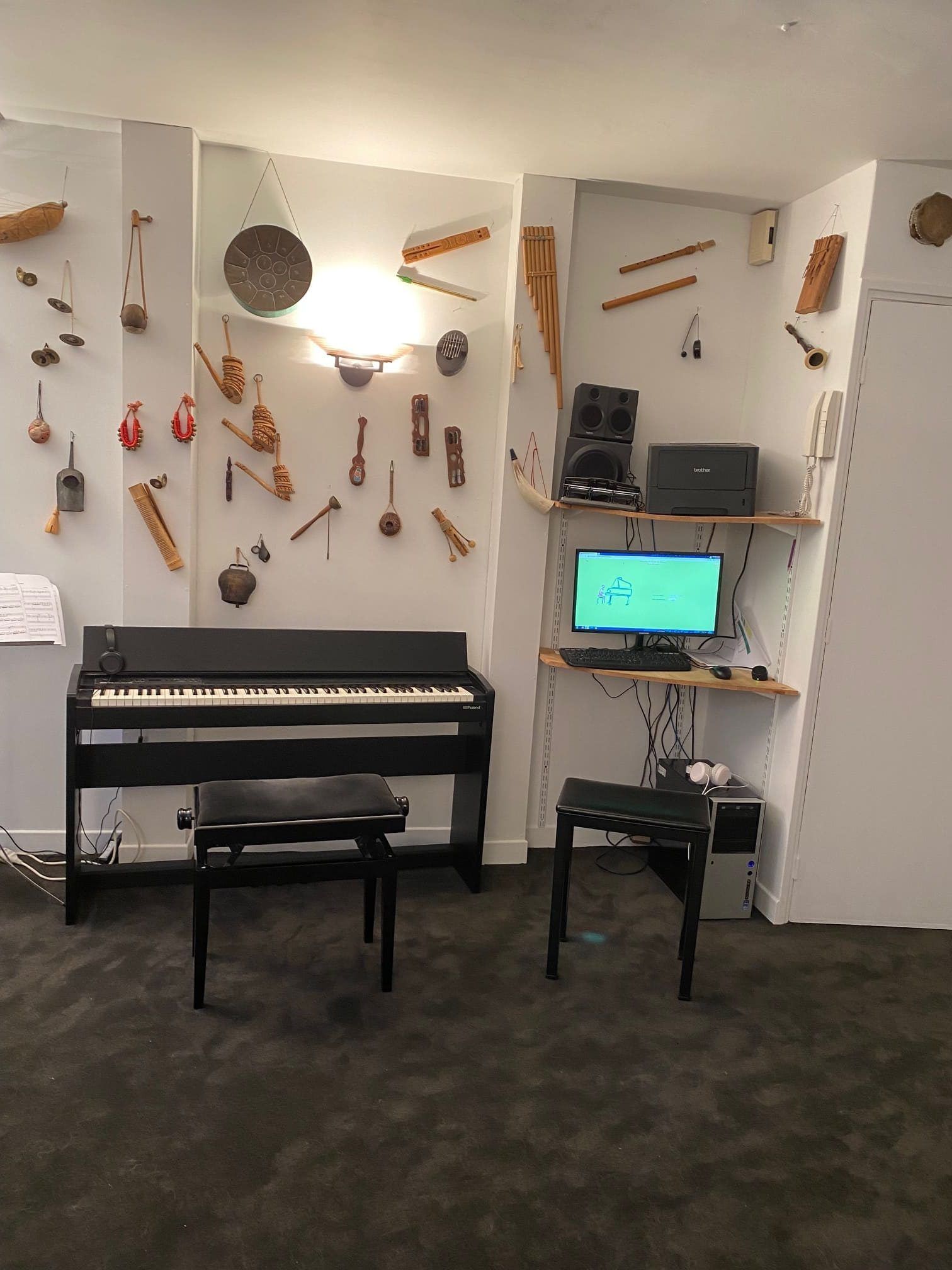 Salle de musique avec piano, ordinateur, haut-parleurs et instruments accrochés au mur.