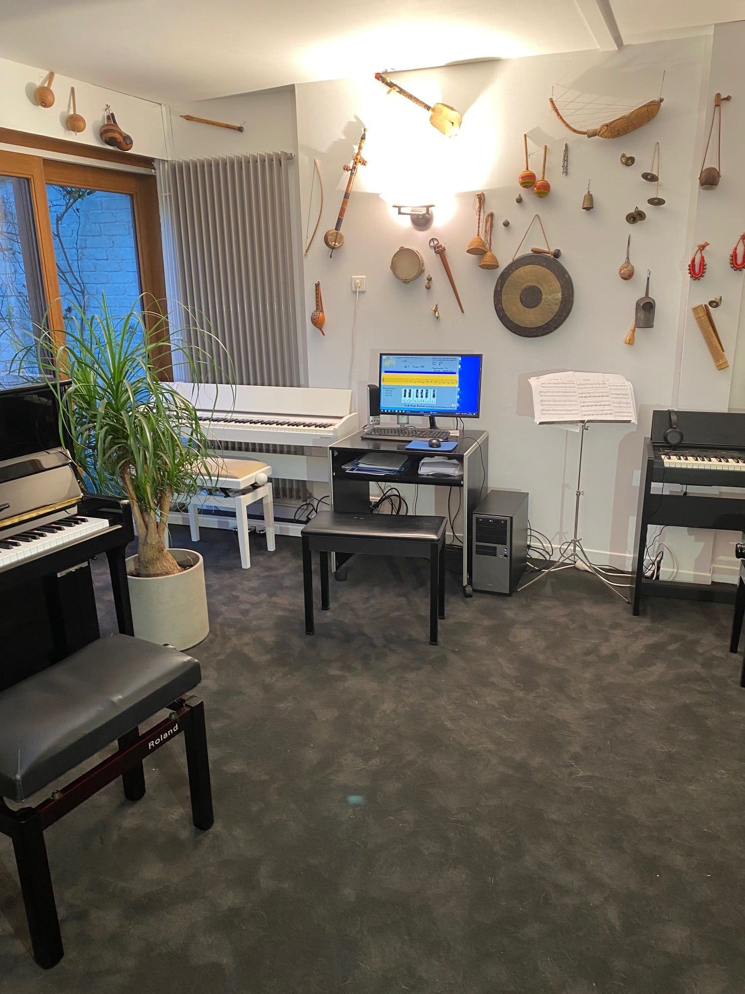 Salle de musique avec des instruments accrochés au mur et des claviers, un ordinateur et un pupitre devant.