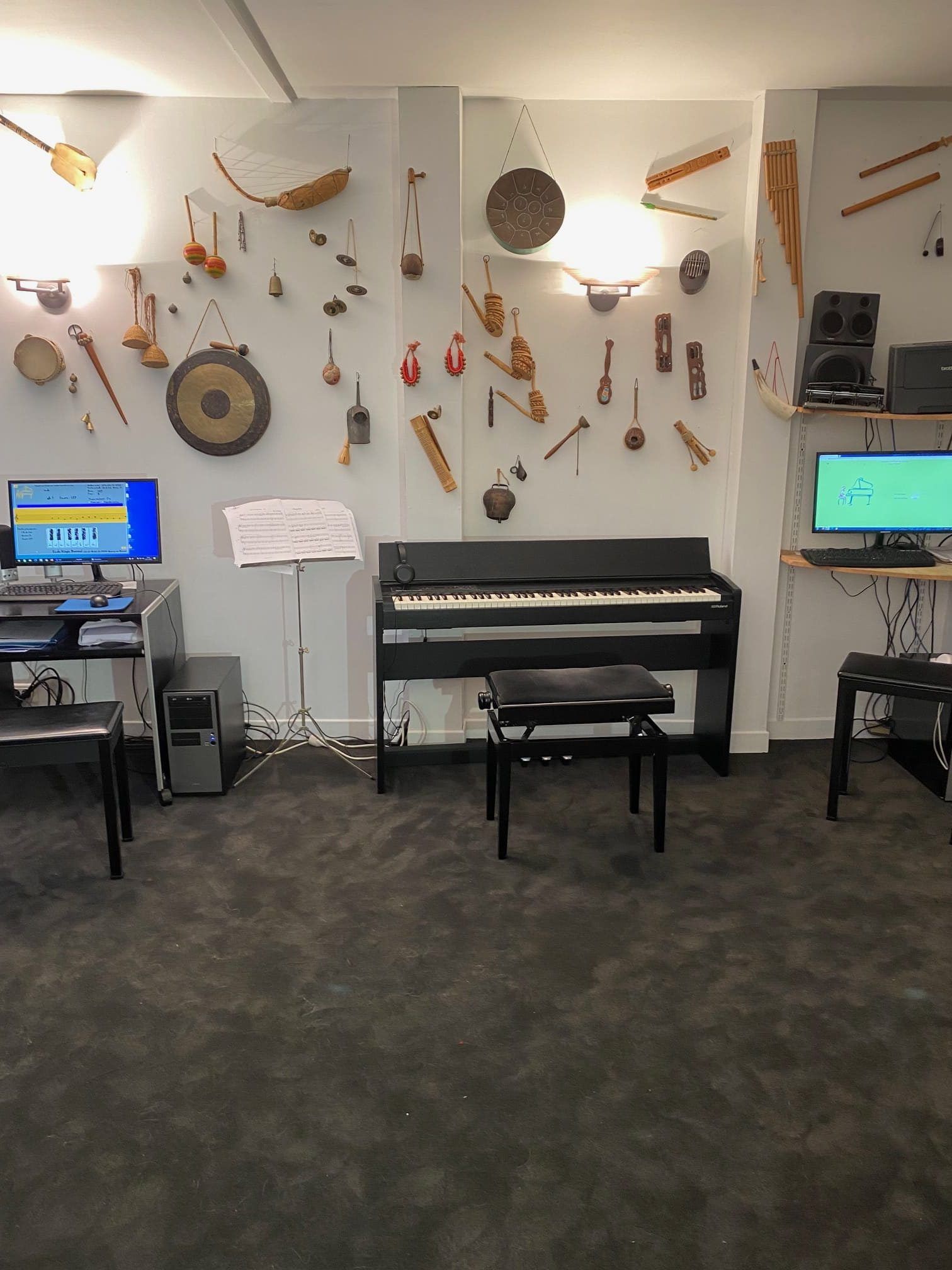 Salle de musique avec piano, ordinateur et de nombreux instruments accrochés au mur.