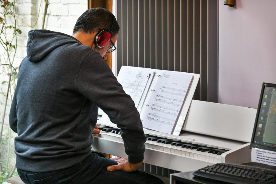 Une personne portant un casque audio joue du piano blanc avec une partition.
