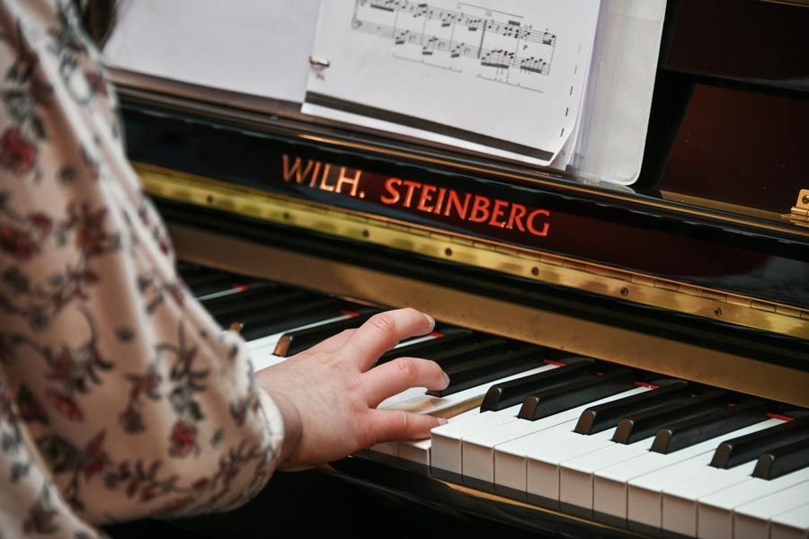 Les mains d'une personne jouant d'un piano noir Wilh. Steinberg, partition sur le pupitre.
