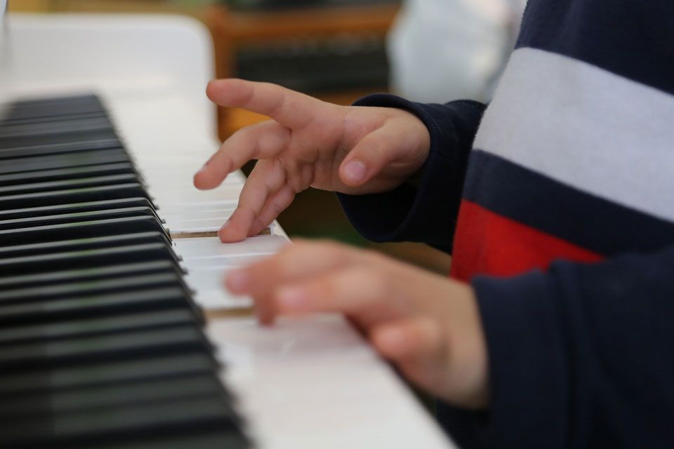 Gros plan sur les mains d'un enfant jouant du piano. On aperçoit une manche à rayures bleues et rouges.