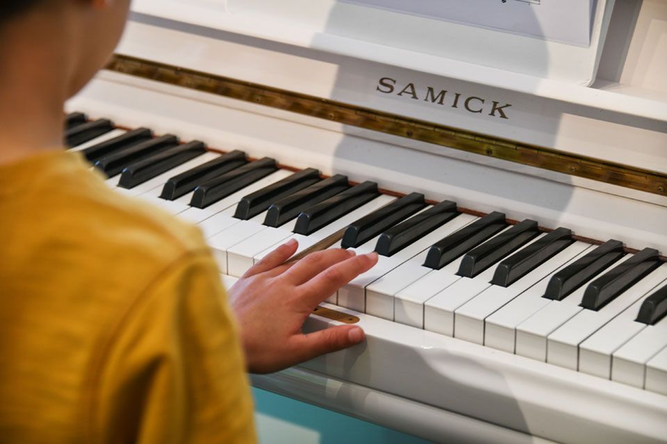 Un enfant joue du piano blanc, la main sur les touches. On aperçoit des bordures dorées et une chemise jaune.