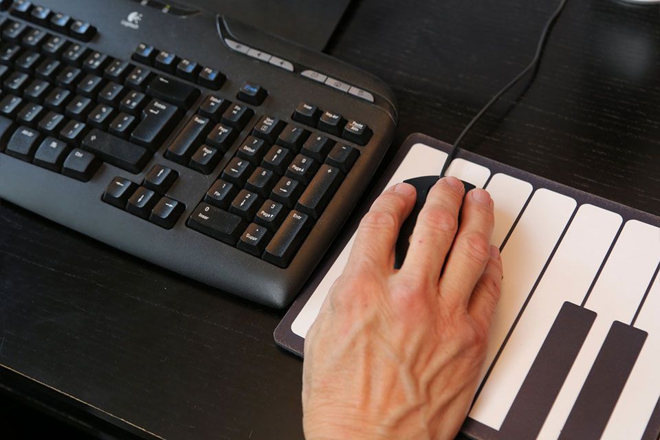 Main utilisant une souris sur un tapis de souris à motif clavier, à côté d'un clavier noir sur un bureau noir.