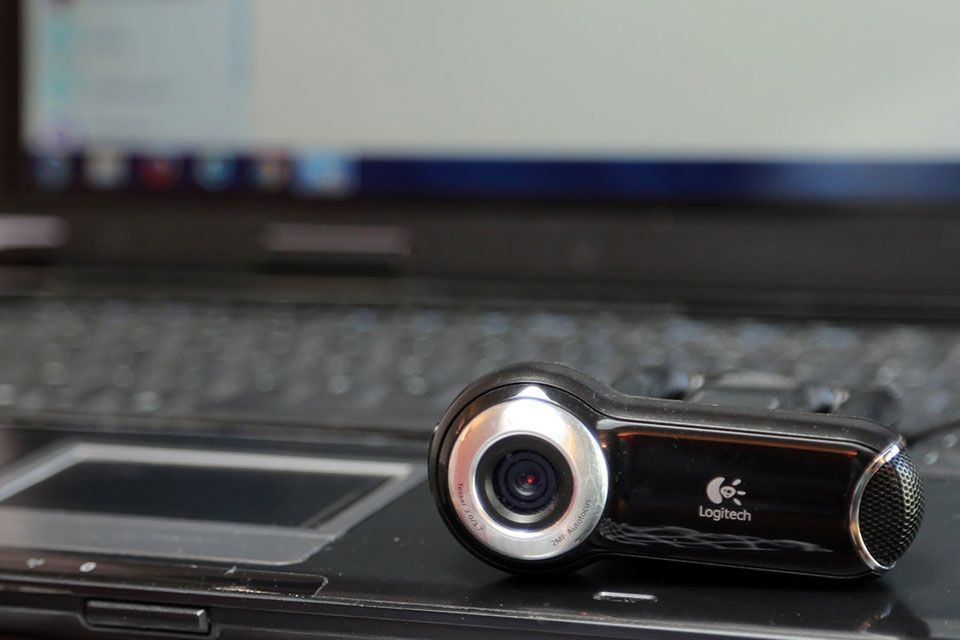 Une webcam Logitech noire est posée sur un ordinateur portable, avec un écran d'ordinateur flou en arrière-plan.