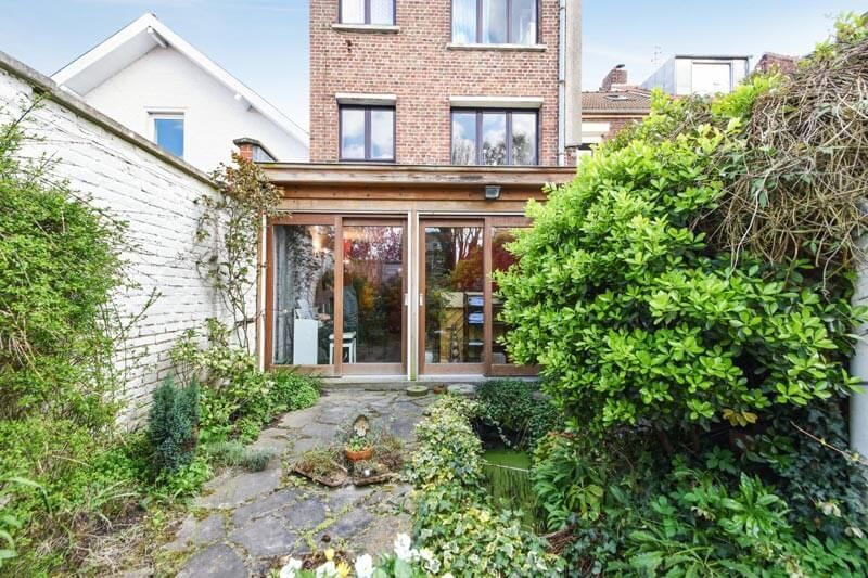 Vue arrière extérieure d'un bâtiment en briques avec une porte vitrée à cadre en bois, entouré d'un jardin.