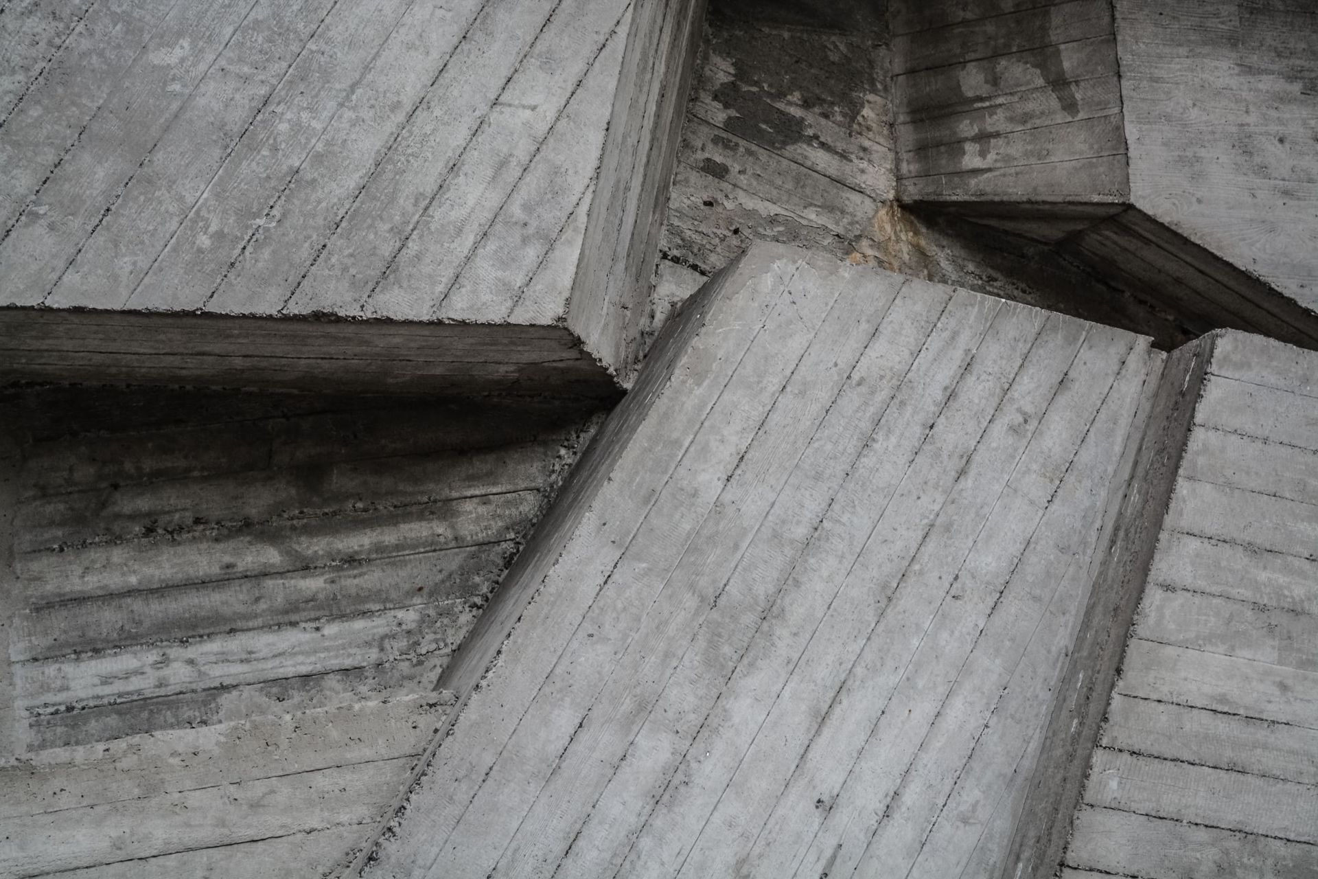 Primer plano de superficies de hormigón texturizadas y geométricas con patrones lineales y variaciones en tonos grises.