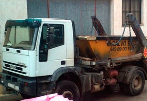 Un camión volquete blanco con un contenedor de basura amarillo en la parte trasera está estacionado frente a un edificio.
