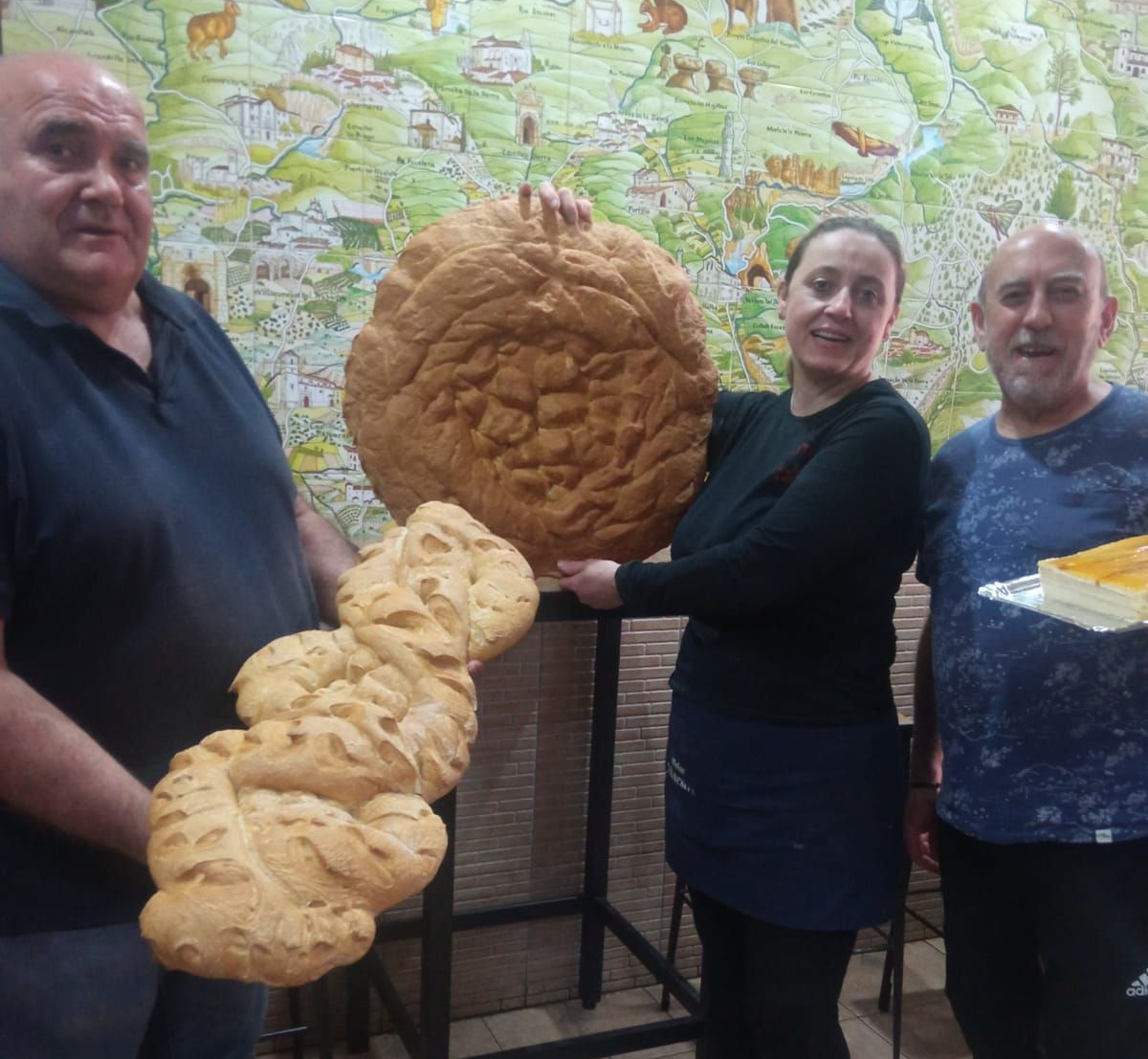 Tres personas están de pie frente a un mapa mural ilustrado, sosteniendo 