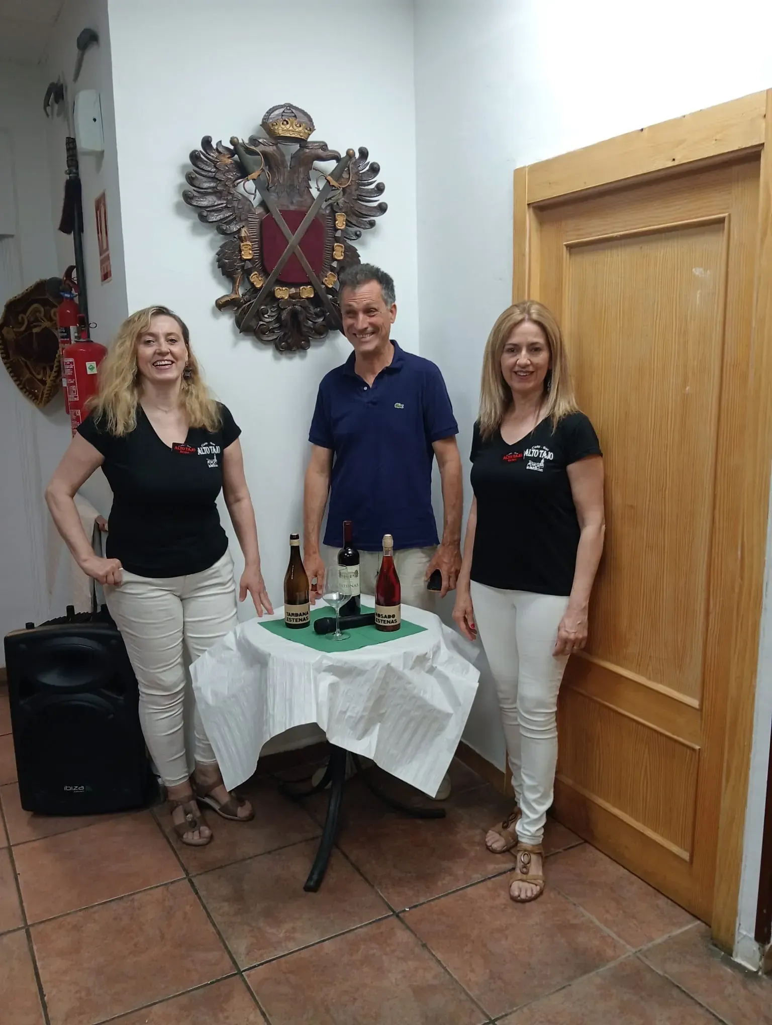 Tres personas están de pie alrededor de una pequeña mesa con tres botellas