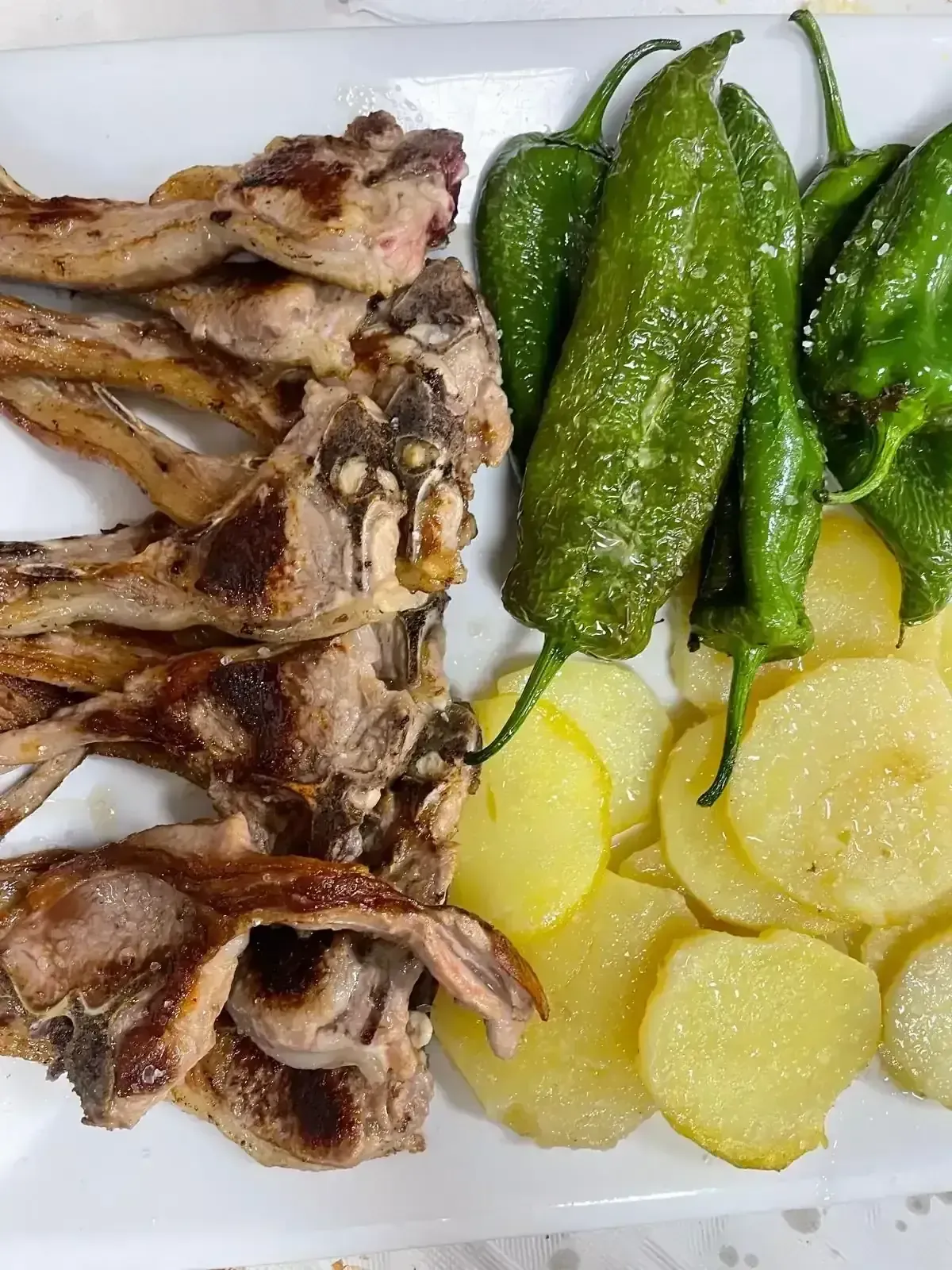 Un plato de chuletas de cordero a la parrilla con patatas en rodajas y pimientos 