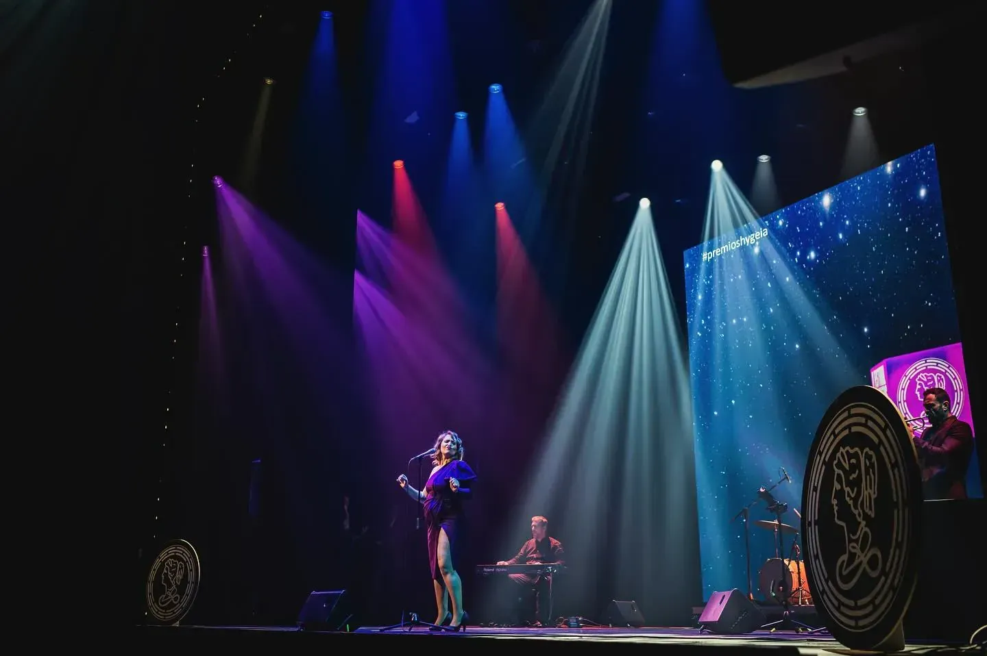 Un cantante actúa en el escenario con luces de colores, miembros de la banda y un fondo estrellado.