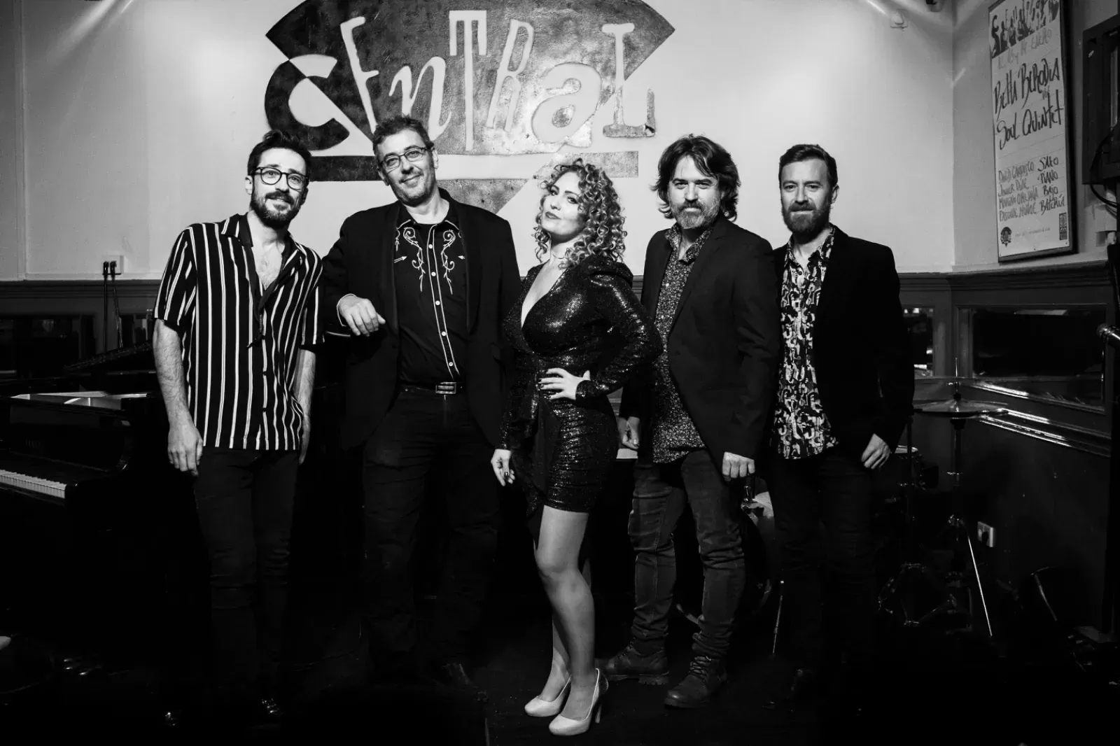 Banda de cinco personas en el interior. Una mujer con un vestido brillante, hombres con chaqueta, todos sonriendo.