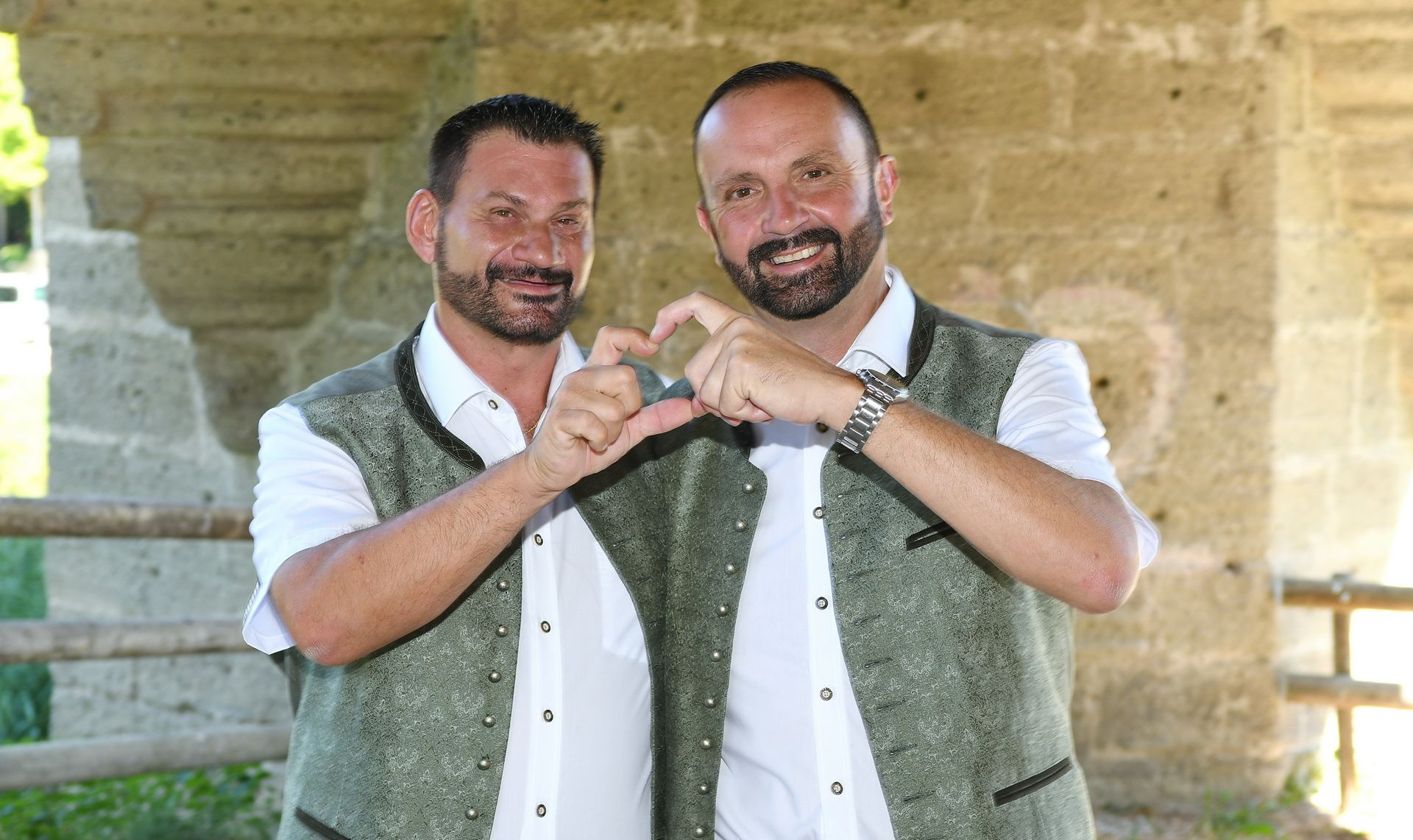 Zwei Bräutigame feiern ihre Hochzeit mit einem Herz aus den Händen