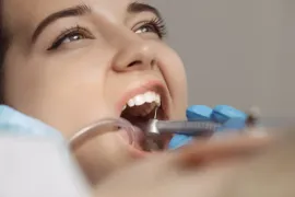 Mujer recibiendo trabajo dental con la boca abierta, un taladro dental y un eyector de saliva colocado.