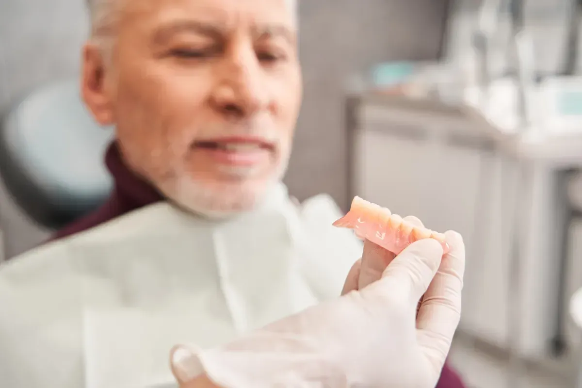 Dentista sosteniendo una dentadura parcial para un paciente sentado en una silla dental.