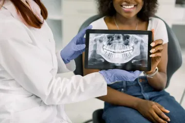 Dentista mostrando a un paciente una radiografía dental en una tableta en un consultorio dental.