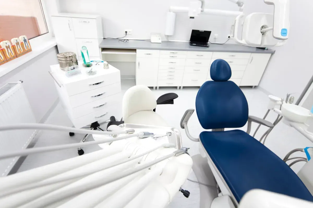Interior del consultorio dental: sillón dental azul y blanco, armarios blancos, equipamiento.