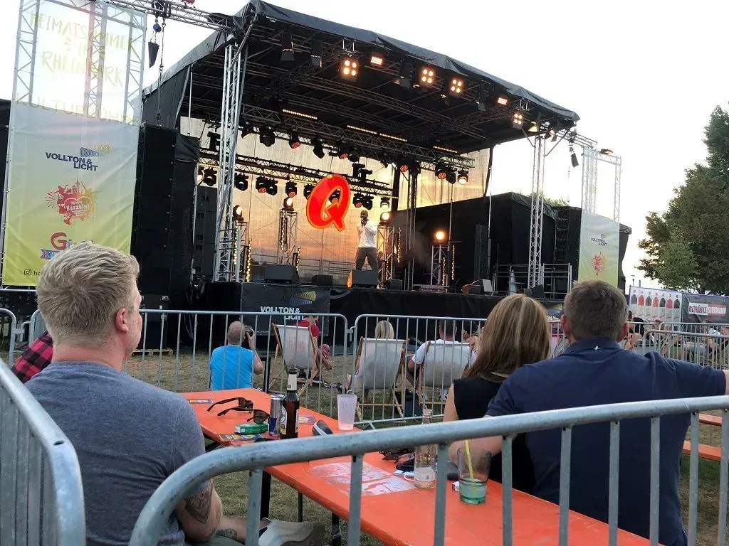 Bei einem Konzert sitzt eine Gruppe von Menschen an Tischen vor einer Bühne.